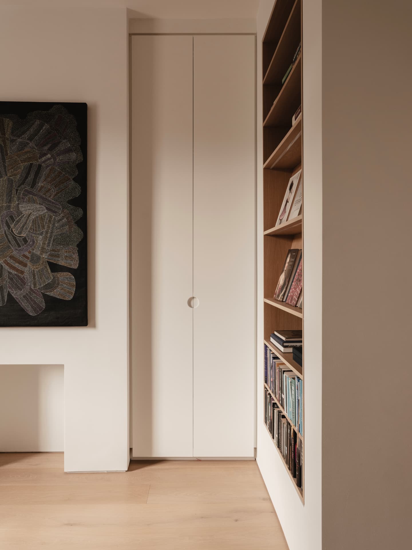 Flush white handleless joinery beside built-in oak shelving and a dark woven textile artwork in a contemporary Dublin interior
