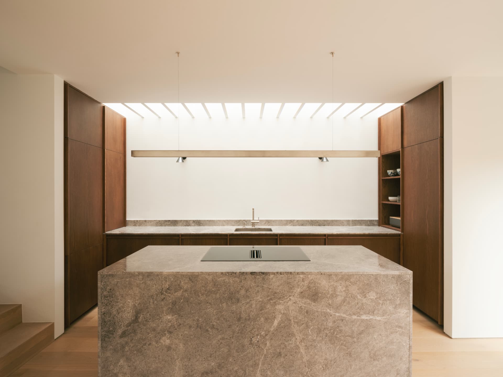 Contemporary kitchen at Greenville Terrace with a honed stone island beneath a slatted skylight, framed by warm timber cabinetry