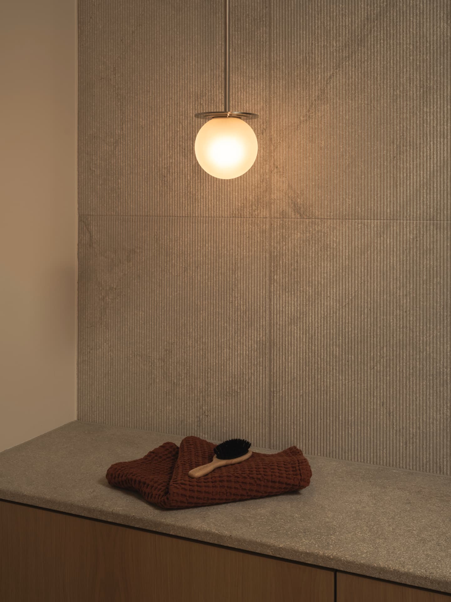 Glowing glass pendant light above a folded rust waffle-cotton towel and timber brush on a stone bench